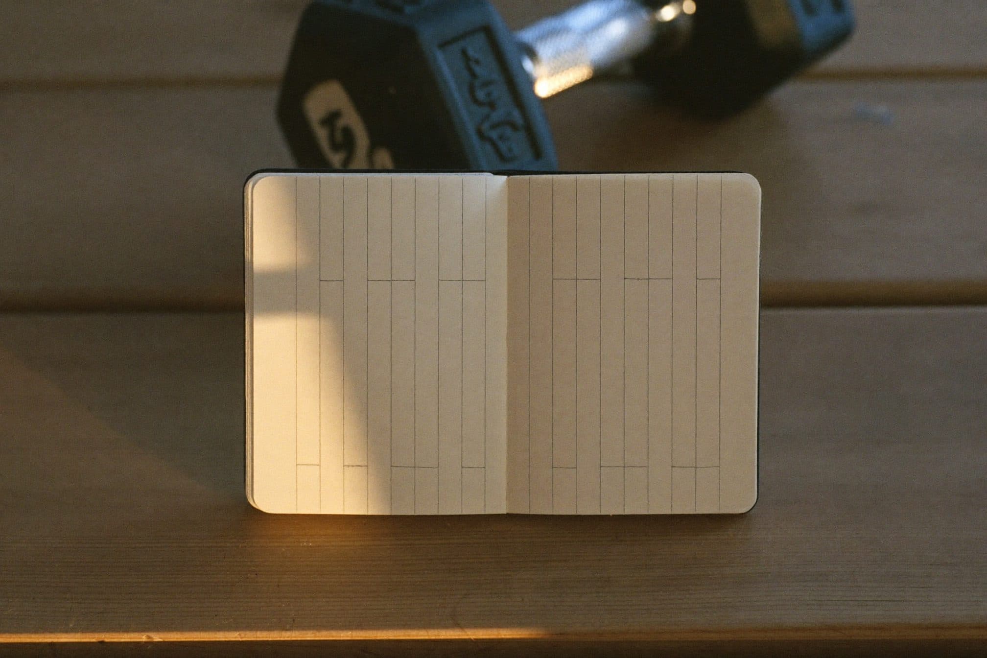 A pocket notebook open on a wooden gym bench with a hex dumbbell in soft focus behind it