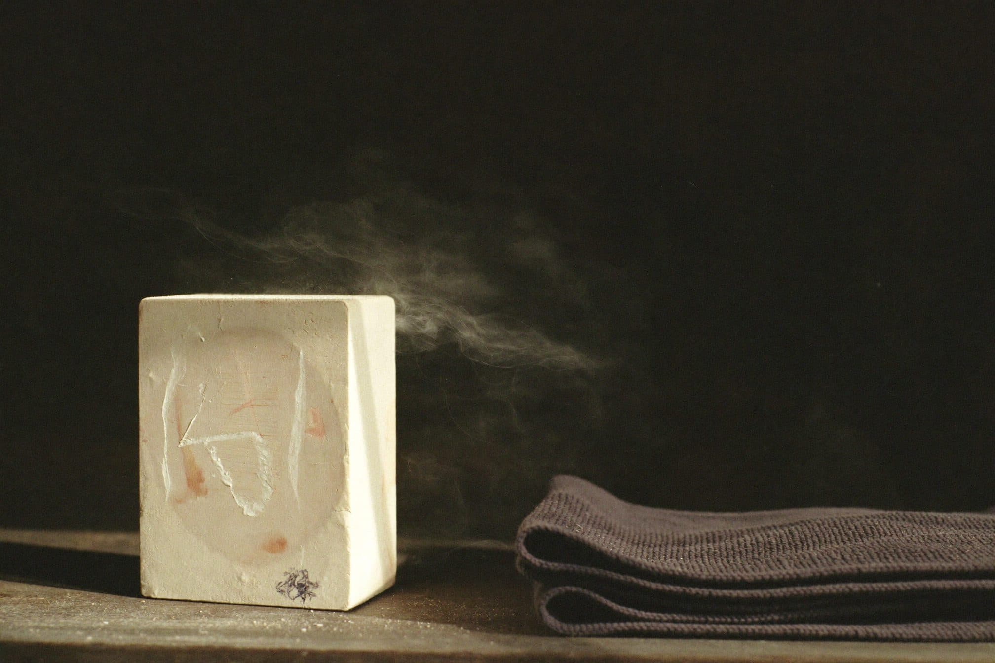 A chalk block and folded gym towel on a dark shelf, chalk dust hanging in a warm beam of light