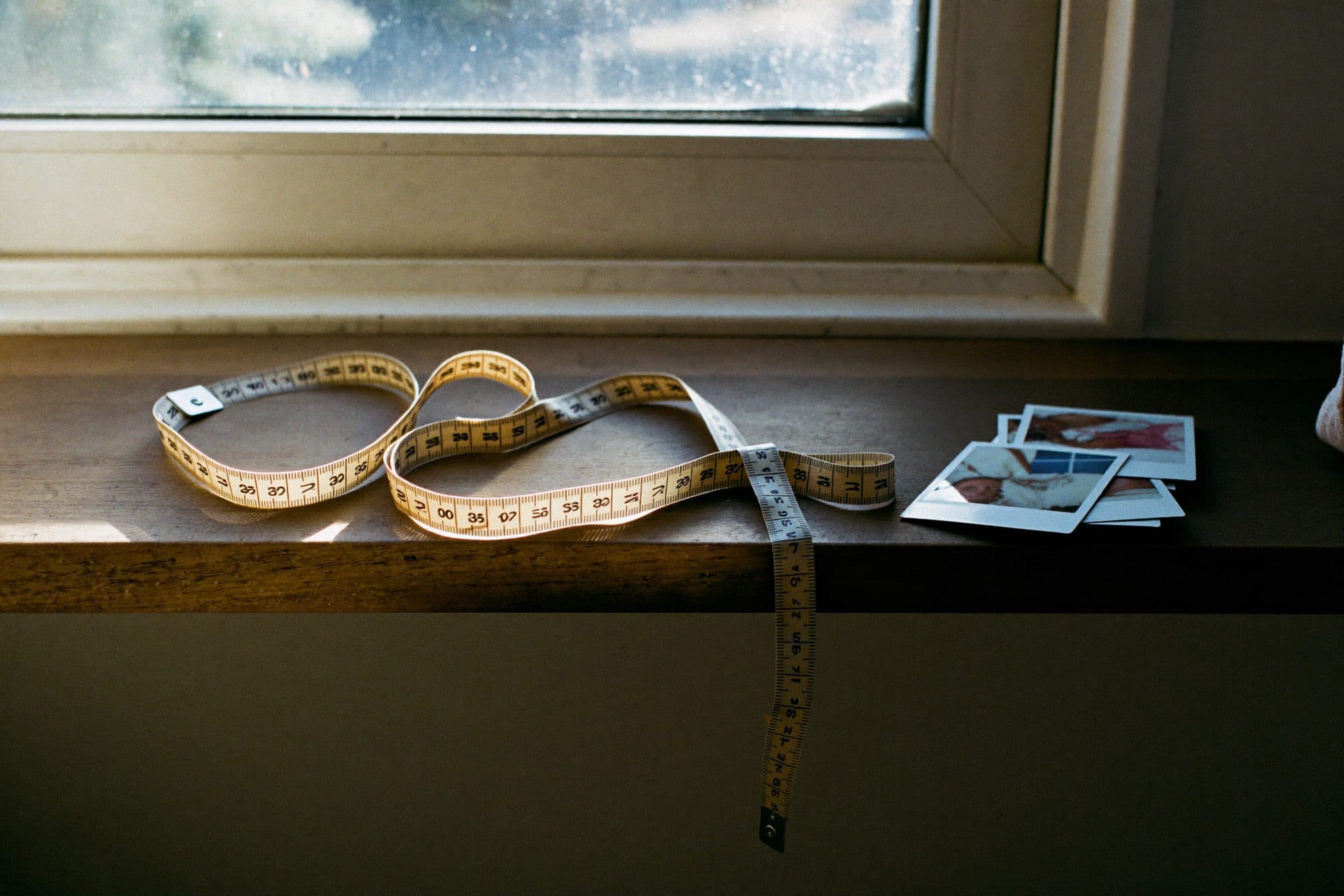 A cloth tape measure coiled on a wooden shelf beside instant photos lying face down