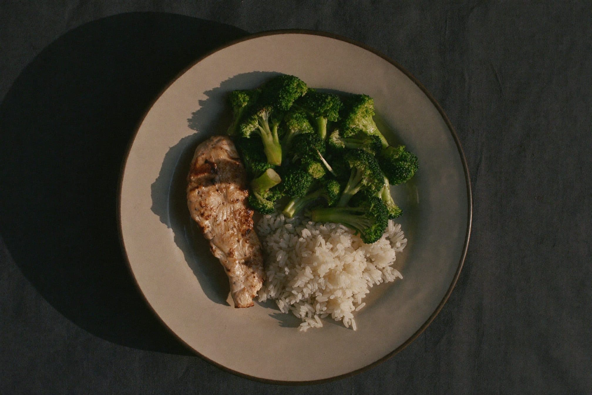 Overhead view of a dinner plate with grilled chicken, roasted broccoli, and a small mound of rice
