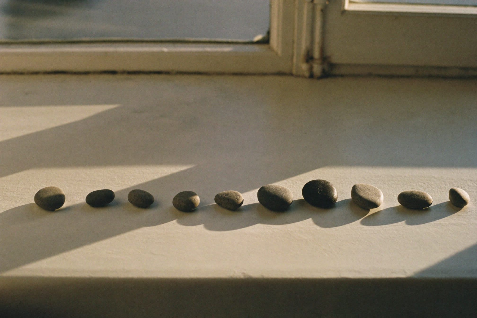 Small smooth pebbles lined up on a white windowsill in warm morning light