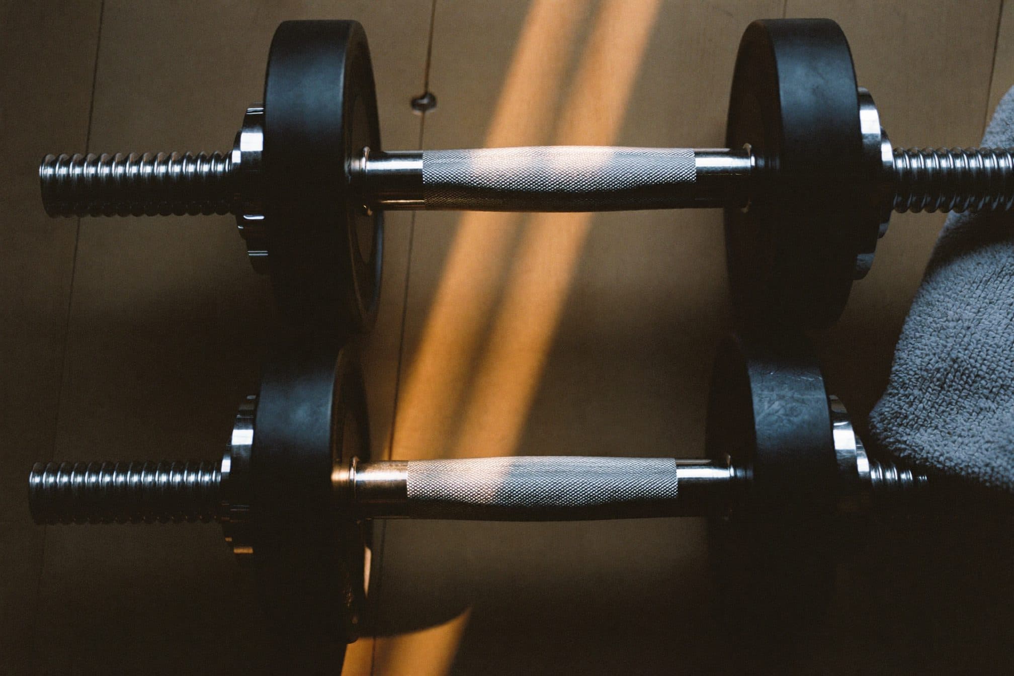 Knurled steel dumbbell handles in a low warm stripe of morning sun, folded towel beside