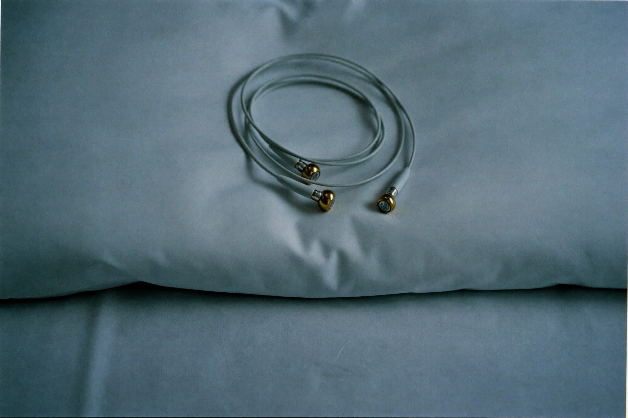 A coil of thin clinical EEG electrode leads with gold cup electrodes on a white hospital pillow