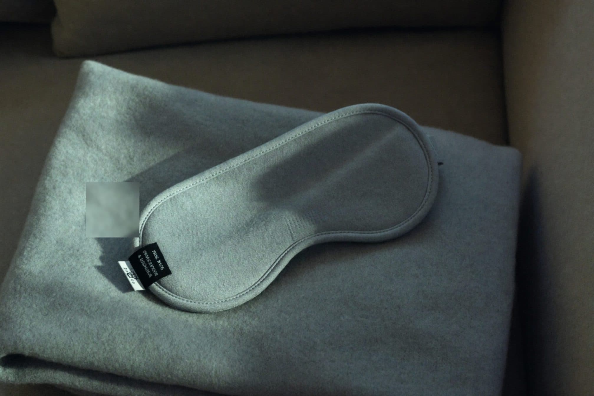 A plain grey sleep eye mask on a folded wool blanket in cool afternoon shade