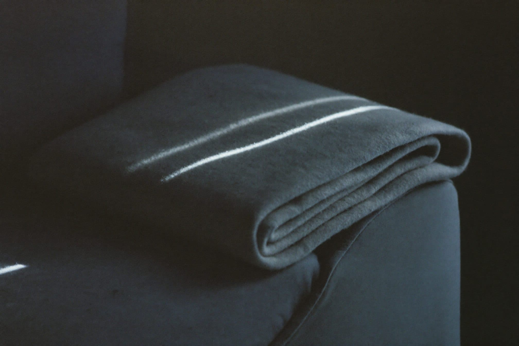 A folded wool blanket on a couch corner with one narrow slice of afternoon light across it