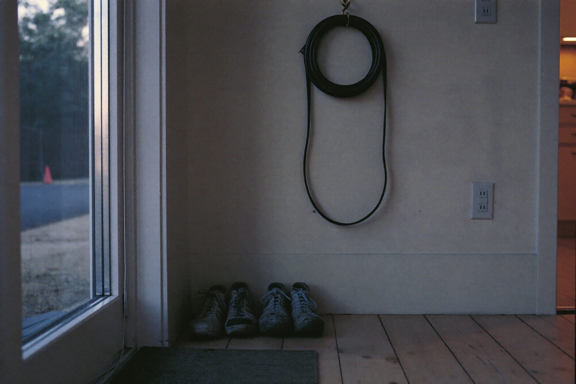 Walking shoes on a plain mat and a coiled dog leash on a hook by a back door at dusk