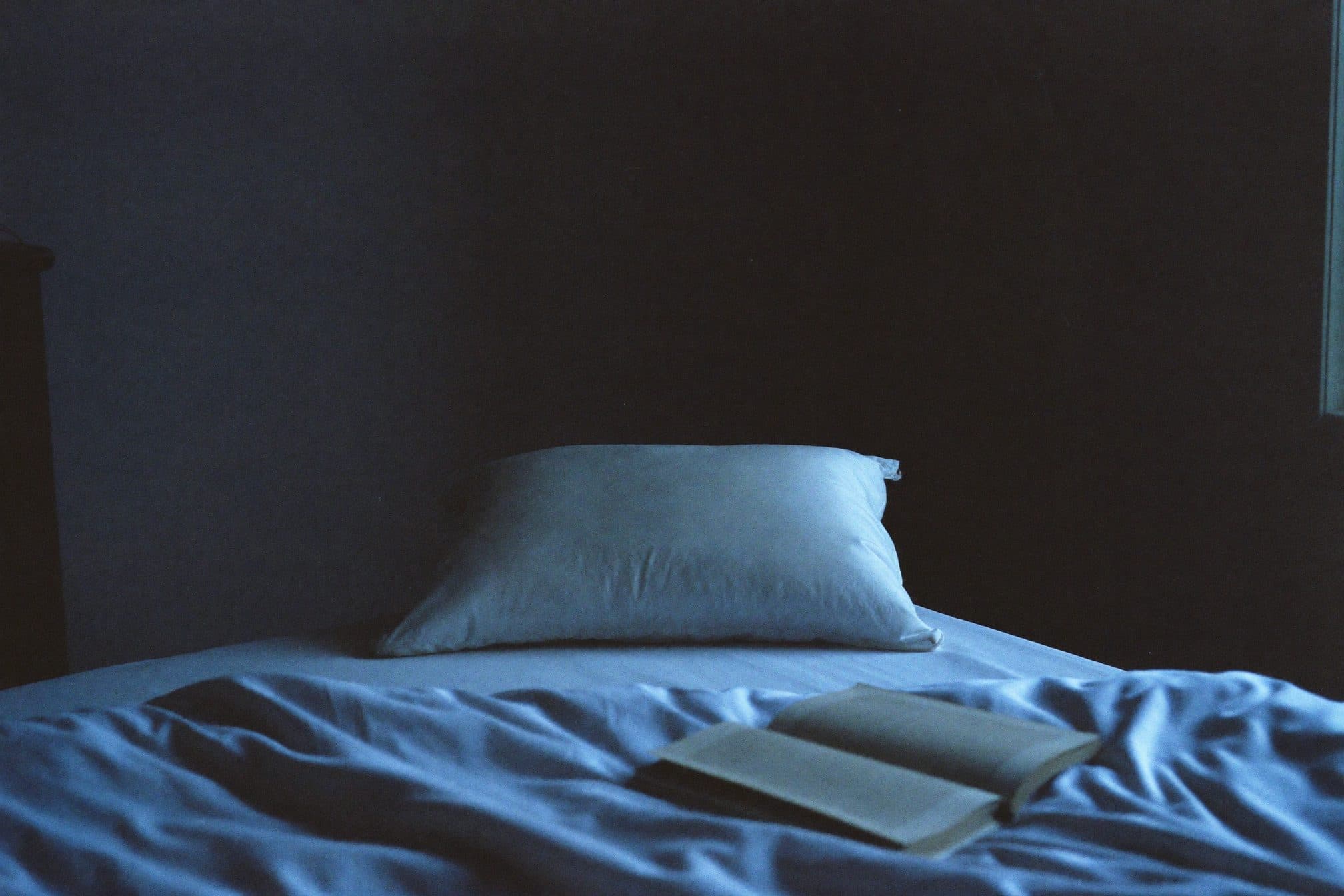 A white pillow at the head of a bed in cool blue evening window light